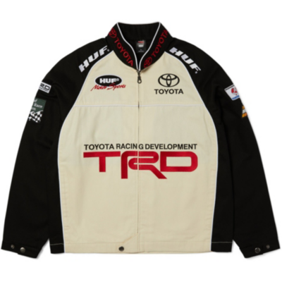 A beige racing jacket with black sleeves. The front has the Toyota logo, ""Toyota Racing Development"" text, and a red ""TRD"" logo. ""Toyota"" and ""HUF"" logo on the chest