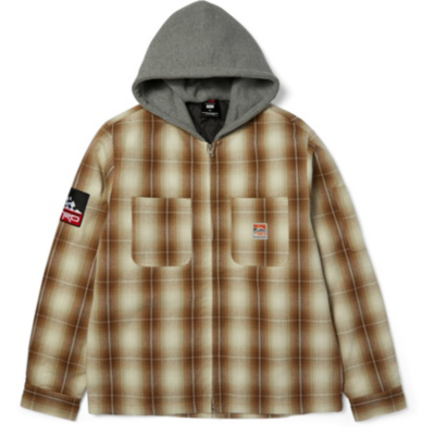 A brown and beige plaid flannel jacket with a gray hood. The jacket has two chest pockets and a black HUF logo on the left sleeve with red and white text.