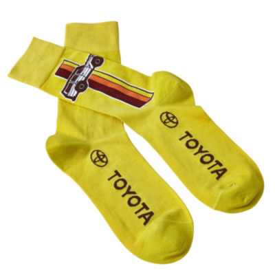 Yellow socks with the word ""TOYOTA"" and the Toyota logo printed in black, featuring  an image of a vintage car with red, orange, and yellow stripes behind it.