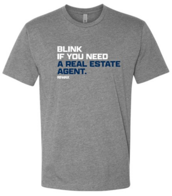 Gray short‑sleeve T‑shirt with the text “BLINK IF YOU NEED A REAL ESTATE AGENT.” printed in white and blue, with the RE/MAX logo beneath the text.