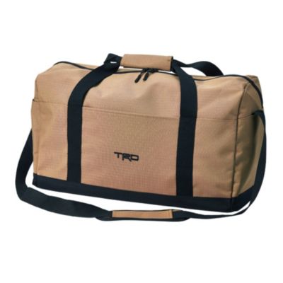 Tan duffel bag with black straps and shoulder strap. The front has a small rectangular patch with ""TRD"" embroidered in black. 