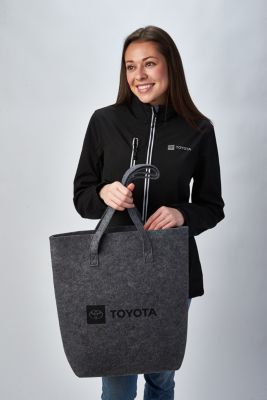 Person in black Toyota jacket holding grey Toyota tote bag