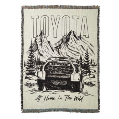 A woven blanket featuring a black and white illustration of a Toyota truck in front of two large mountains with trees around it.