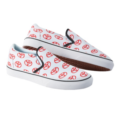 A pair of white slip-on sneakers with a pattern of red Toyota logos printed all over. The shoes have black piping around the edges and white soles with a brown rubber bottom
