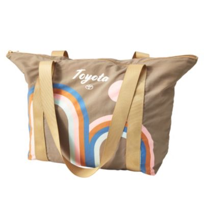 A beige tote bag with two handles and a zipper closure. The bag features a colorful rainbow design in blue, orange, pink, and white. Above the rainbow design is the Toyota logo
