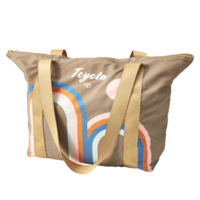 A beige tote bag with two handles and a zipper closure. The bag features a colorful rainbow design in blue, orange, pink, and white. Above the rainbow design is the Toyota logo
