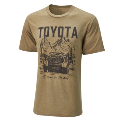 A tan-colored T-shirt featuring a graphic design with the word 'TOYOTA' in large, bold letters at the top. Below it is an illustration of a Toyota truck driving through a forest and text that reads 'At Home In The Wild.