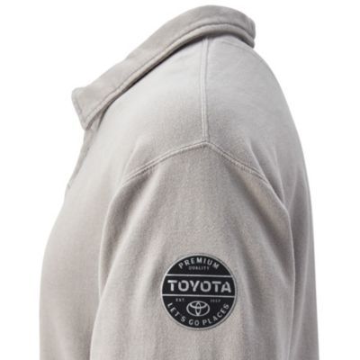 Upper part of a light grey collared shirt featuring a circular patch on the sleeve with the text 'PREMIUM QUALITY' at the top, 'TOYOTA' in the center, 'LET'S GO PLACES' at the bottom, and the Toyota logo within the patch.