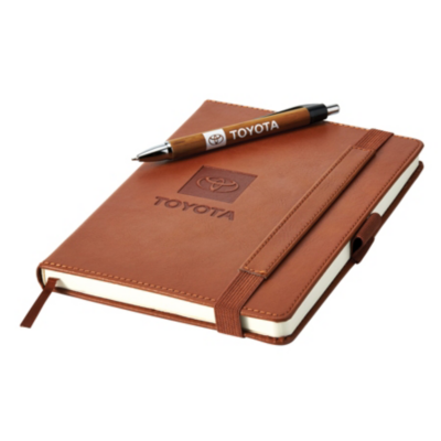 A brown leather-bound notebook with an elastic strap and pen loop, featuring the Toyota logo and 'TOYOTA' embossed on the cover. A matching pen is placed diagonally across the top