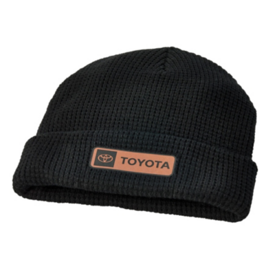 A black knit beanie hat with a folded brim and a brown patch with Toyota on it.