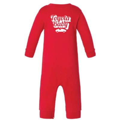 A red baby onesie with long sleeves and legs. The back of the onesie features white text that reads Toyota Baby above a small white car graphic