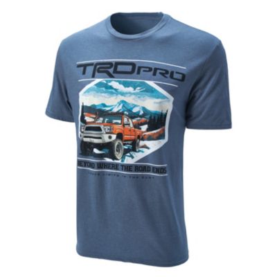 A blue T-shirt featuring a graphic design of an orange off-road vehicle driving through a mountainous landscape with pine trees. The text 'TRD Pro' is displayed prominently above the graphic.