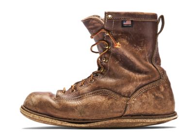 A well worn brown leather work boot with scuffs and a thin outsole.