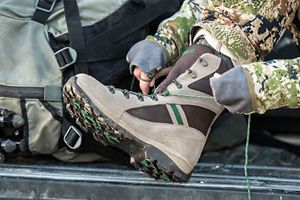 a woman laces up her grey and green hunting boots