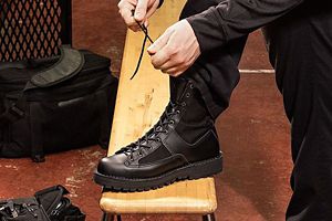 a woman laces up her black tactical boots in a locker room