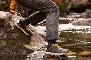 a man hikes against the backdrop of alpine lake wearing brown and red hiking boots