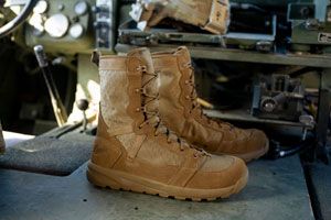 a pair of coyote colored military boots sits alongside a gas can and some tactical gear