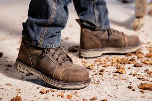 a pair of brown work boots with orange laces caked in mud