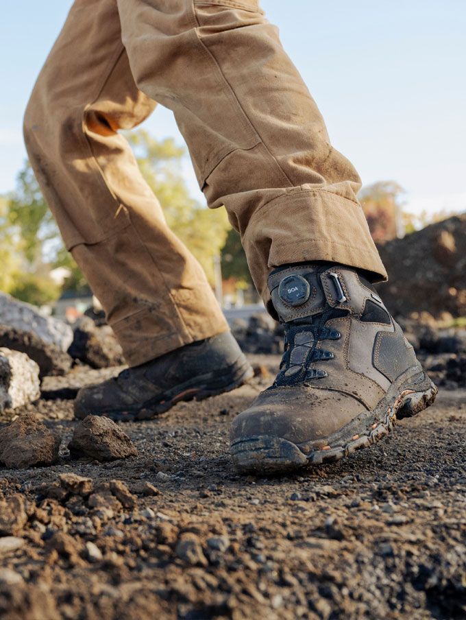 a worker climbs into a backhoe while wearing brown work boots
