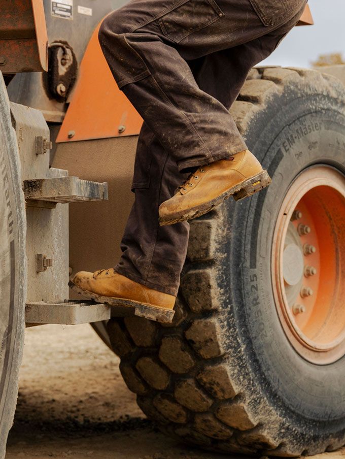 a worker climbs into a backhoe while wearing brown work boots