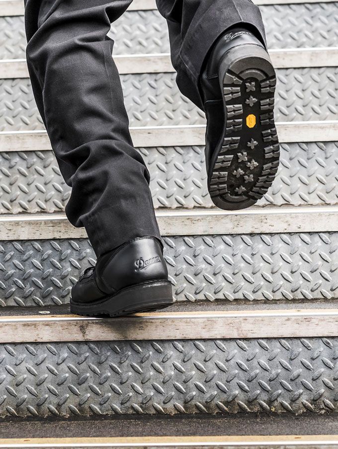 A person walks briskly up a metal staircase wearing polished black leather uniform boots and black pants