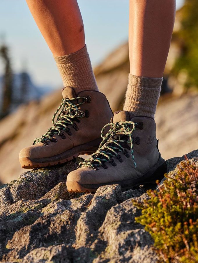 A hiker stands on a rock wearing gray boots illuminated by low evening sunlight in a dry landscape, a pause after a long day on the trail