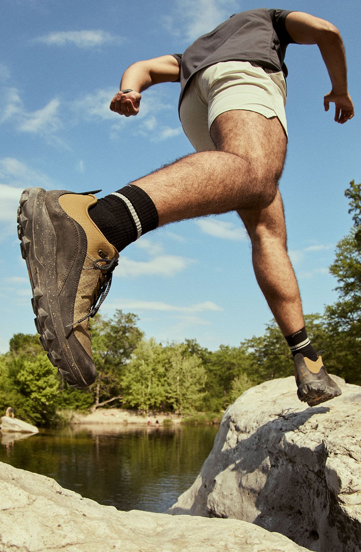 A man in shorts scrambling across rocks while wearing coyote and black hiking shoes