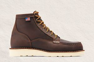 a man laces up a pair of brown hunting boots with a moc toe design