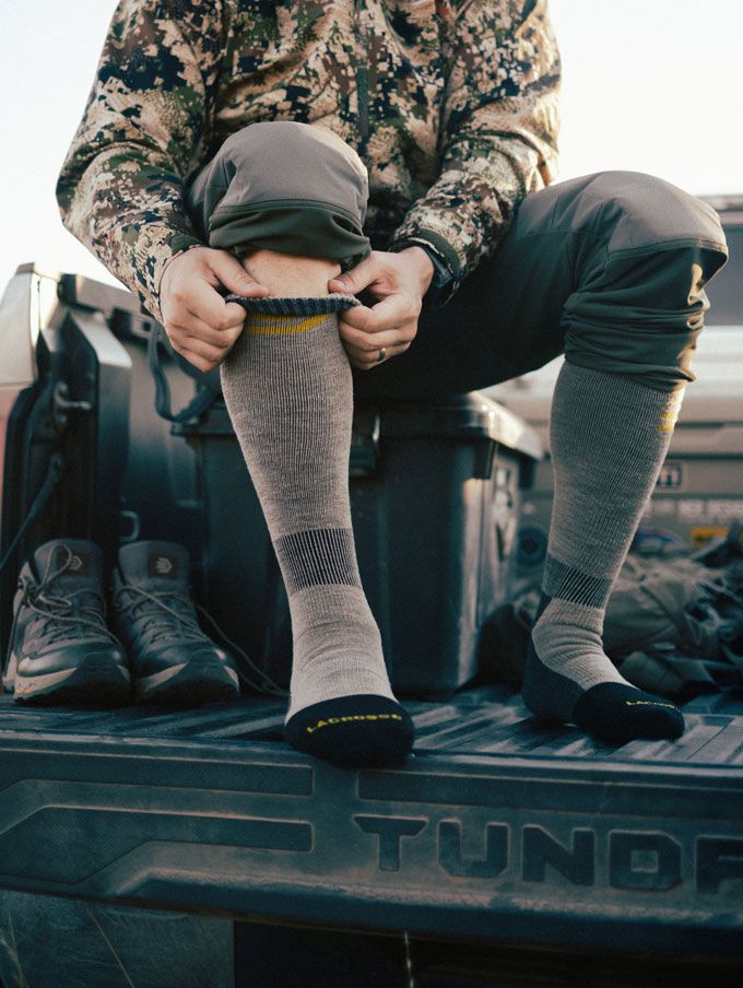 A man sits on a cooler in the back of his pickup while pulling up his knee high socks