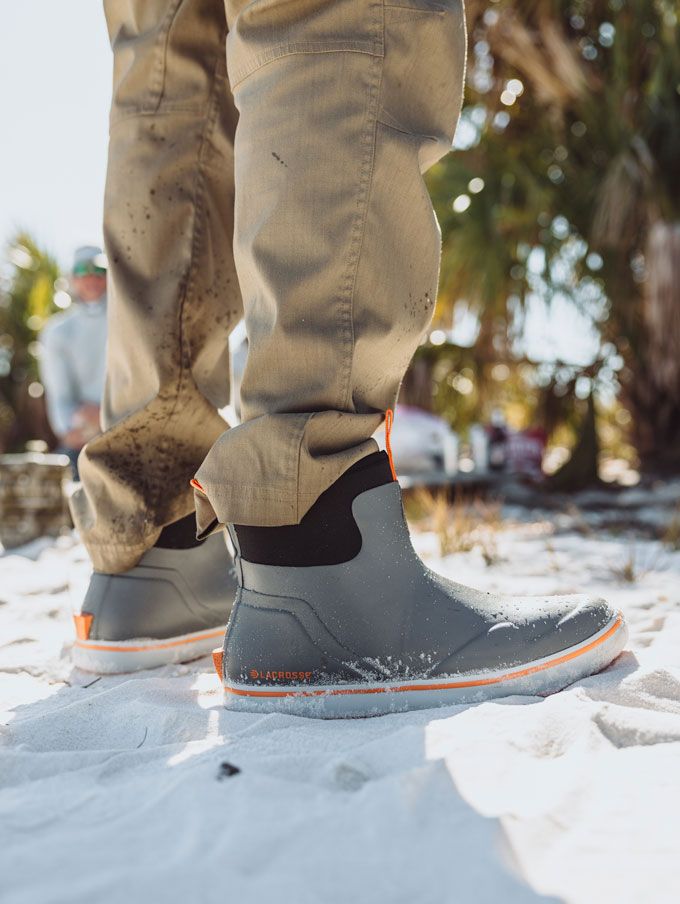 a man stands in the sand wearing tan outdoor pants and gray and orange deck boots