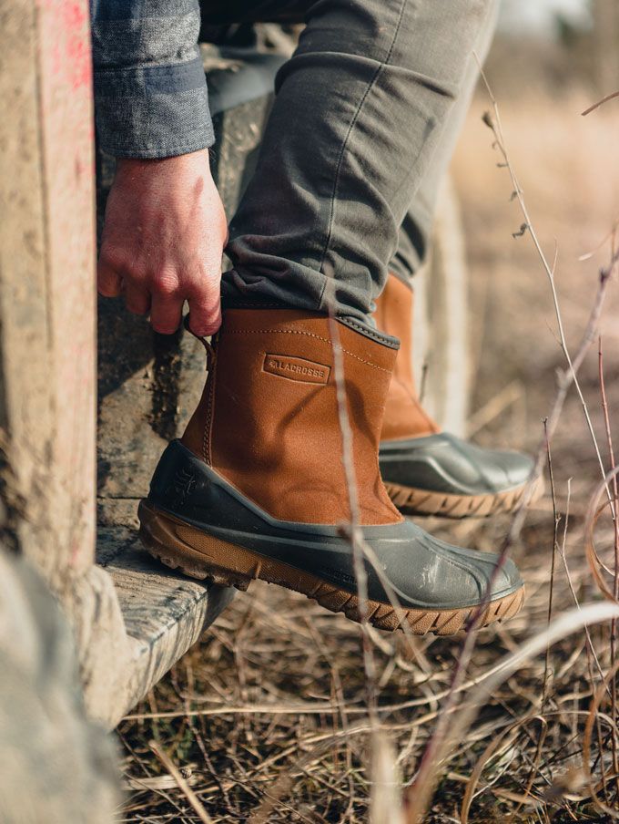 A pair of rubber and leather duck boots being pulled up by the tab on the back of the boots