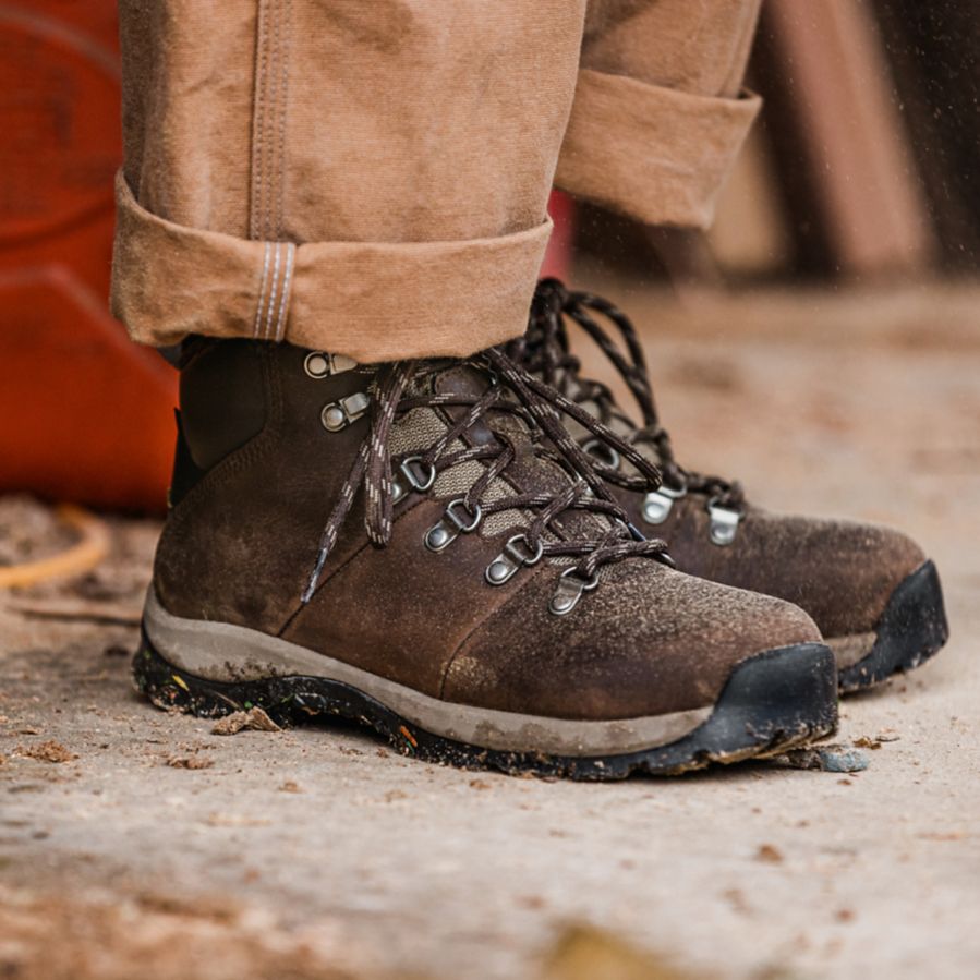 Close up of a woman’s feet as she stands on a sawdust-covered concrete floor wearing brown pants and dark brown leather boots.