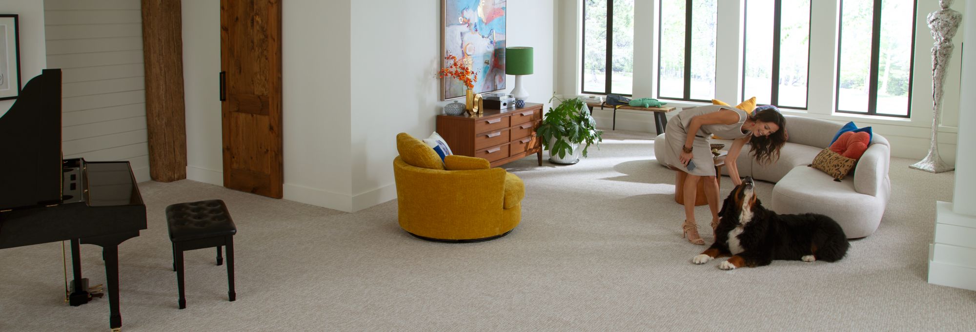 Karastan Smartstrand logo overlayed over a living room scene with grey carpet and a woman petting her dog