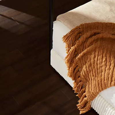 Blanket draped over a bed on top of Karastan wood floors