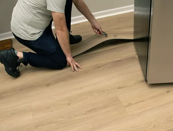 man pulling up hardwood floor plank with pliers