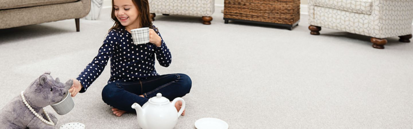 girl having a tea party with a toy rhino wearing a pearl necklace