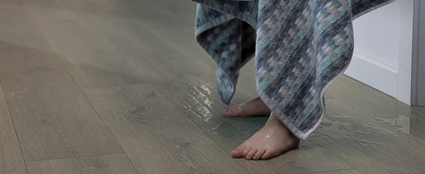 Wet feet on top of flooring with a towel being held