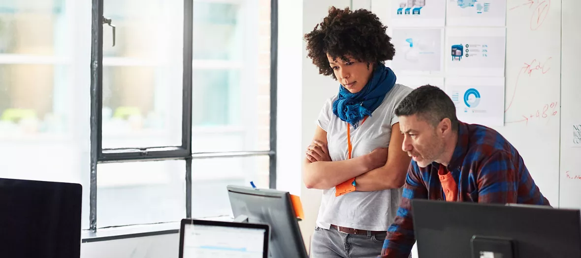 A businessman and businesswoman working together on a computer in a tech start-up office