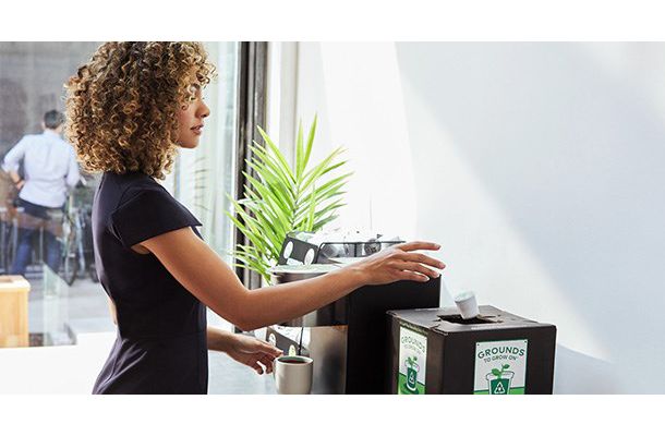 Professional Woman at her office, recycling a used K-Cup Pod by placing it in a Grounds to Grow On Box next to the brewer